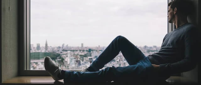Grass is Greener Syndrome - Anxious man sitting by window Grass is Greener Syndrome - Anxious man sitting by window