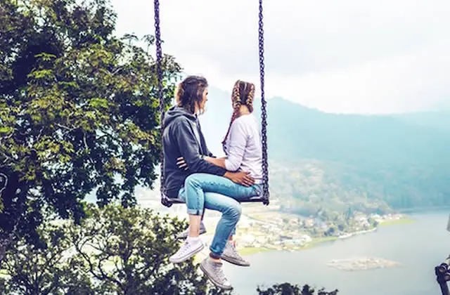 Couple on mountain swing looking at ocean below