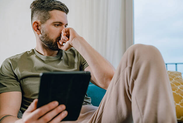 No Contact Rule-Importance and Effectiveness-Sad guy in thoughts sitting on a sofa with a tablet in his hand No Contact Rule-Importance and Effectiveness-Sad guy in thoughts sitting on a sofa with a tablet in his hand