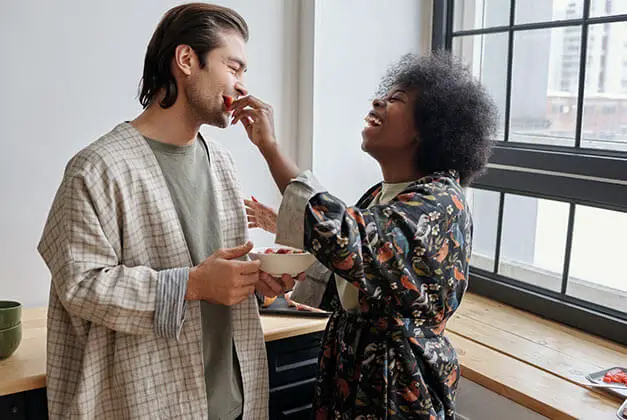 How To Make Him Feel Happy - Laughing lady feeding her man in the kitchen