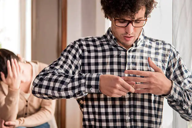 Why Men Pull Away - Guy removing wedding ring from finger with sad wife in the background Why Men Pull Away - Guy removing wedding ring from finger with sad wife in the background