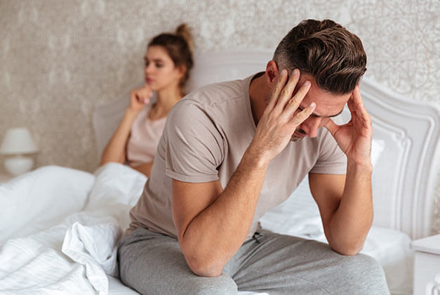 Women That Cheat - Sad man sitting on bed with his girlfriend on background at home Women That Cheat - Sad man sitting on bed with his girlfriend on background at home