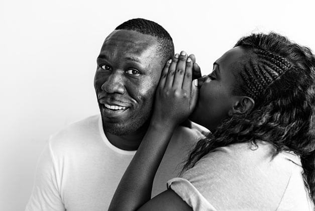 How to Communicate Effectively With a Man - Young African-American lady whispering into her smiling husband's ear How to Communicate Effectively With a Man - Young African-American lady whispering into her smiling husband's ear