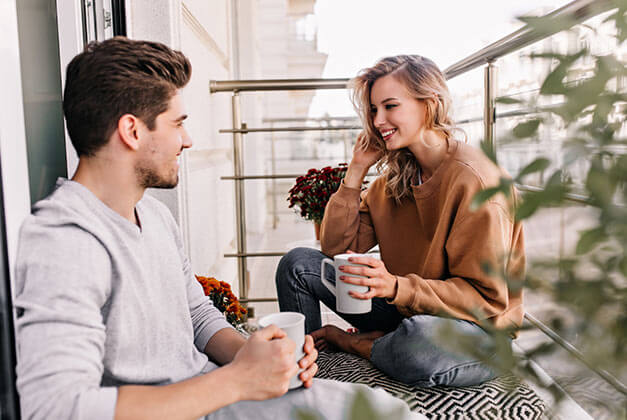 Understanding How Men Communicate - Happy couple talking on balcony drinking tea Understanding How Men Communicate - Happy couple talking on balcony drinking tea